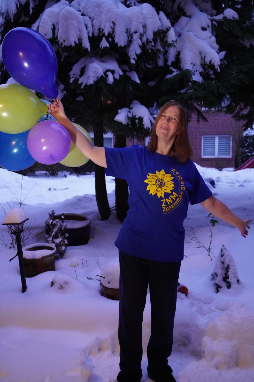 Bettina im ZNM-Vereinsshirt steht draußen im Schnee mit vielen bunten Luftballons in der Hand.